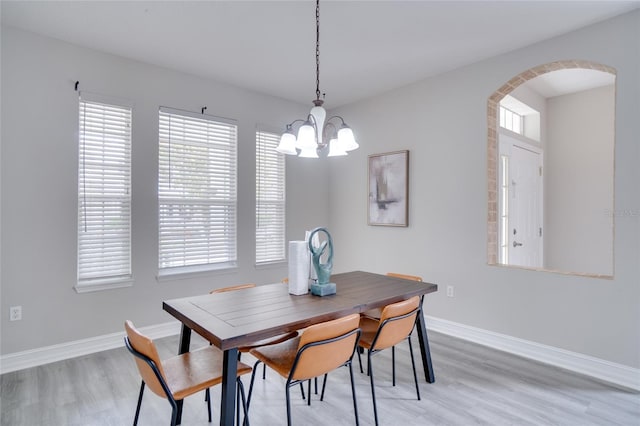 dining room with arched walkways, a notable chandelier, a wealth of natural light, and light wood finished floors