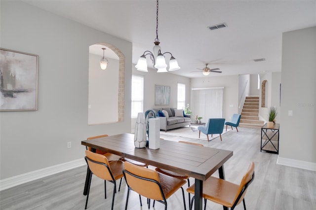 dining room with stairway, arched walkways, light wood-style flooring, and visible vents