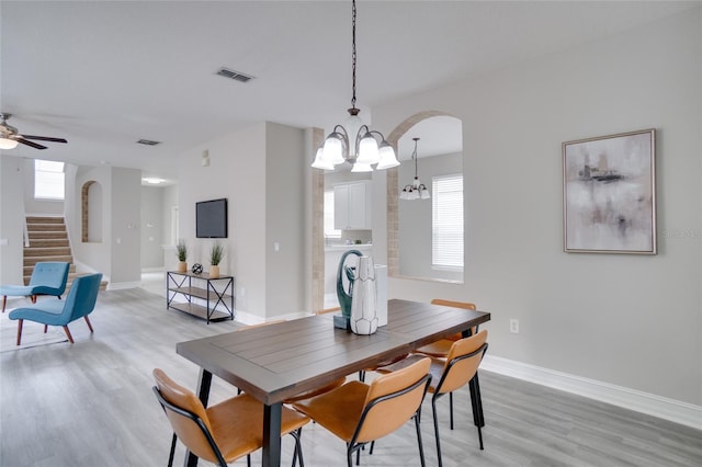 dining space featuring visible vents, a healthy amount of sunlight, light wood-style floors, stairway, and arched walkways
