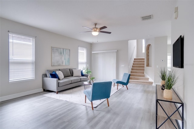 living room with ceiling fan, light wood finished floors, baseboards, visible vents, and stairway