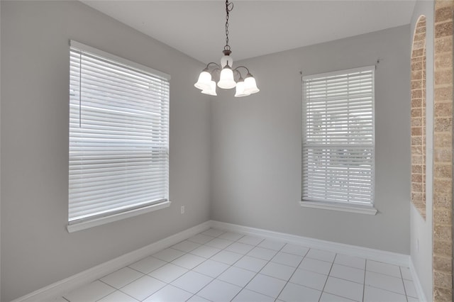 spare room with an inviting chandelier, light tile patterned floors, and baseboards