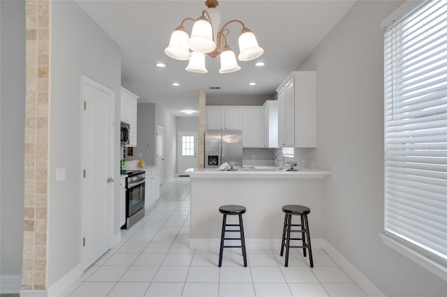 kitchen with white cabinets, appliances with stainless steel finishes, a breakfast bar, an inviting chandelier, and a peninsula