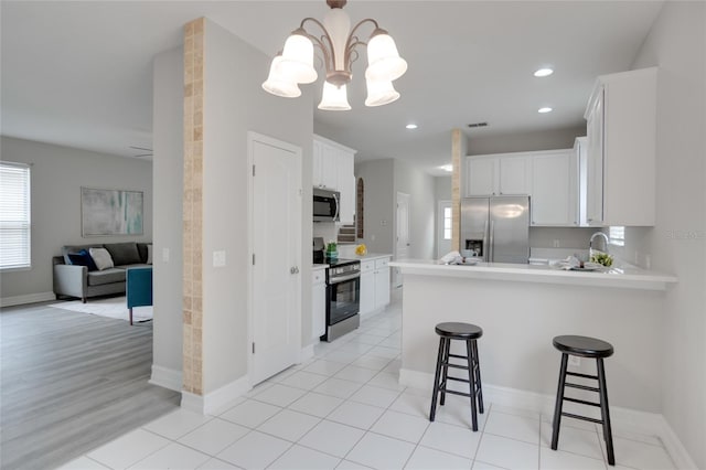 kitchen featuring kitchen peninsula, light hardwood / wood-style floors, stainless steel appliances, white cabinets, and an inviting chandelier