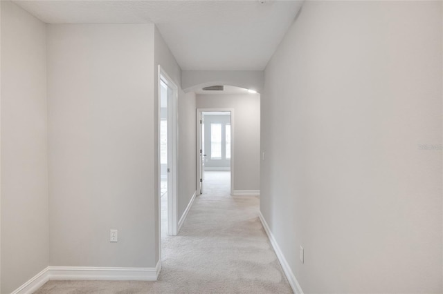 corridor featuring visible vents, arched walkways, baseboards, and light carpet
