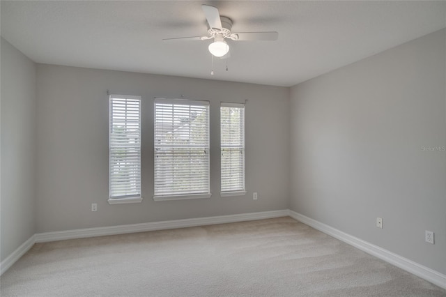 spare room with ceiling fan, light carpet, and baseboards