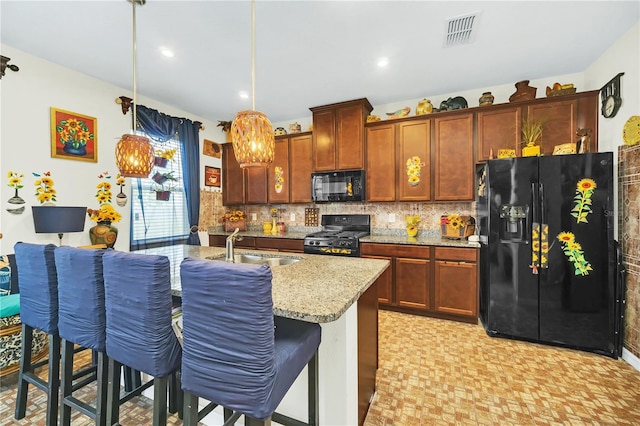 kitchen with a kitchen breakfast bar, light stone countertops, black appliances, sink, and decorative light fixtures