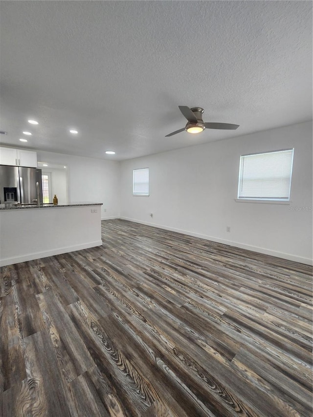 unfurnished living room featuring a textured ceiling, a healthy amount of sunlight, dark wood-type flooring, and ceiling fan