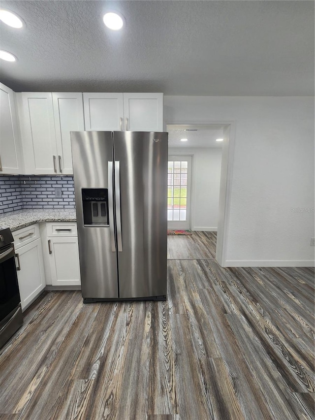 kitchen with stainless steel appliances, backsplash, light stone countertops, white cabinetry, and dark hardwood / wood-style flooring