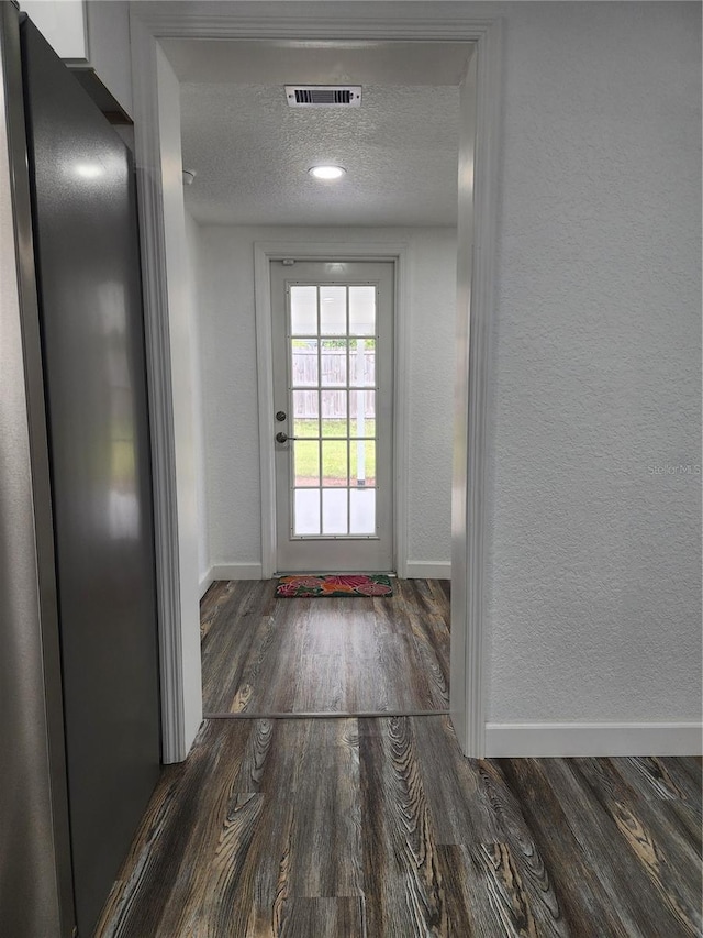 doorway to outside with a textured ceiling and dark wood-type flooring