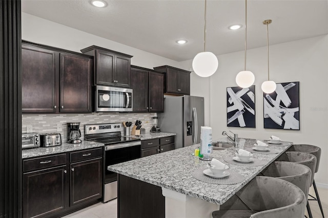 kitchen featuring an island with sink, a breakfast bar, pendant lighting, appliances with stainless steel finishes, and tasteful backsplash