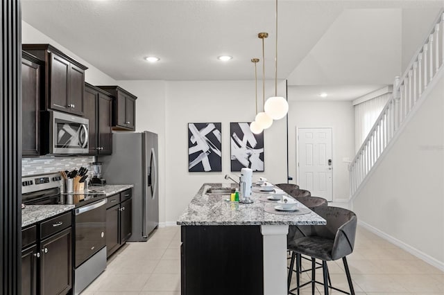 kitchen featuring tasteful backsplash, an island with sink, a breakfast bar, light stone countertops, and stainless steel appliances