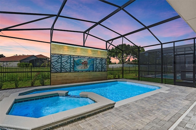 pool at dusk featuring a patio area, an in ground hot tub, and glass enclosure