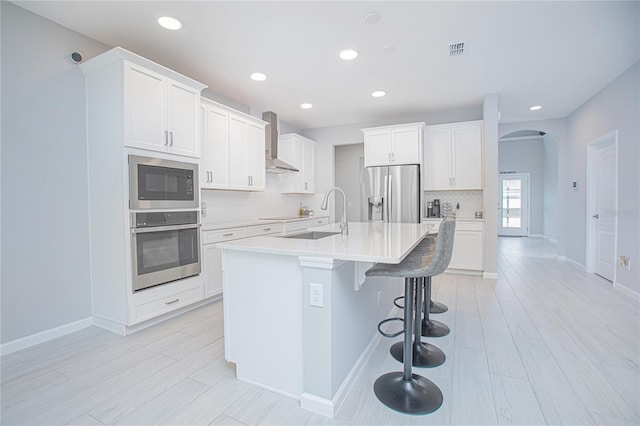 kitchen with sink, white cabinets, wall chimney range hood, and stainless steel appliances