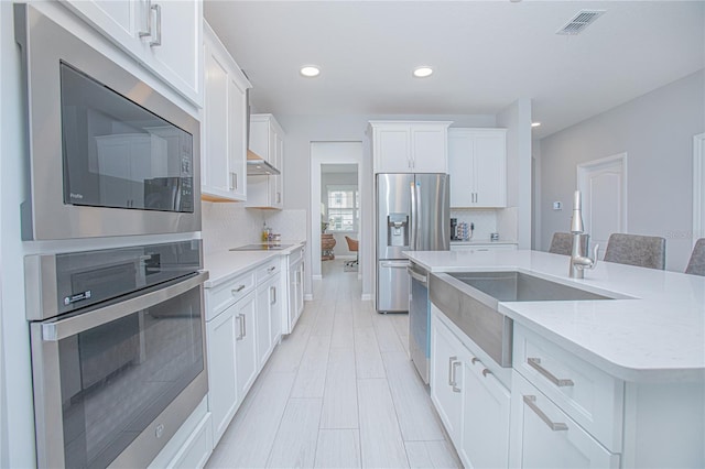 kitchen with an island with sink, a kitchen breakfast bar, white cabinetry, stainless steel appliances, and decorative backsplash