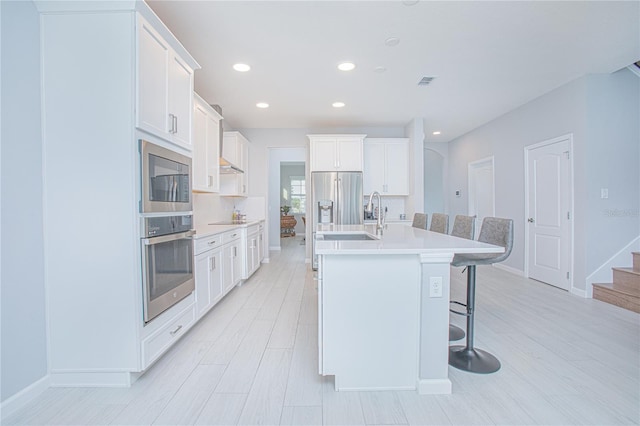 kitchen featuring appliances with stainless steel finishes, white cabinets, and an island with sink