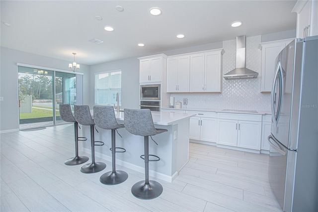 kitchen with white cabinetry, stainless steel appliances, wall chimney exhaust hood, and an island with sink