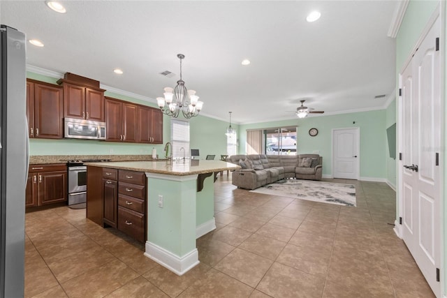 kitchen featuring a kitchen breakfast bar, an island with sink, stainless steel appliances, ornamental molding, and ceiling fan with notable chandelier