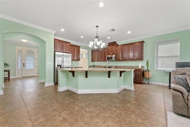 kitchen featuring light stone counters, stainless steel appliances, decorative light fixtures, crown molding, and a breakfast bar area