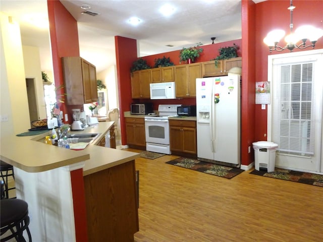 kitchen featuring sink, white appliances, light hardwood / wood-style flooring, decorative light fixtures, and kitchen peninsula