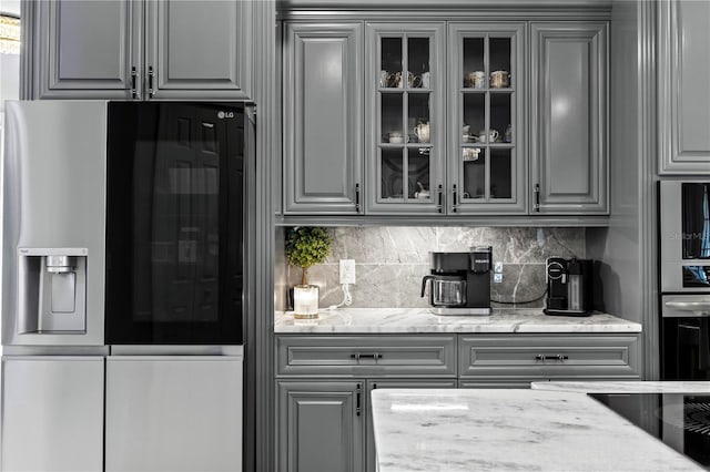 kitchen featuring backsplash, gray cabinets, light stone counters, and stainless steel appliances