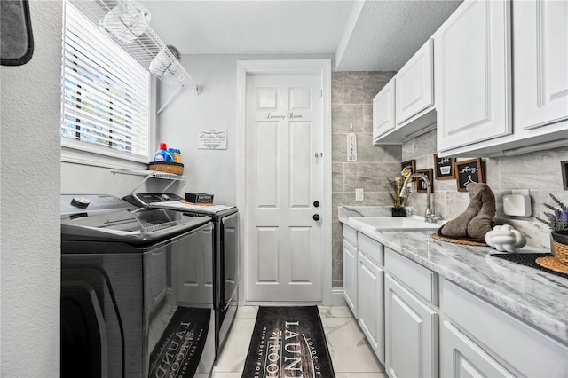 washroom with a textured ceiling, washer and dryer, cabinets, and sink