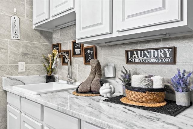 room details featuring white cabinets, tasteful backsplash, light stone counters, and sink