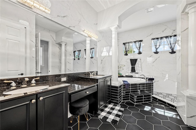 bathroom featuring decorative columns, tiled tub, tile patterned floors, vanity, and tile walls