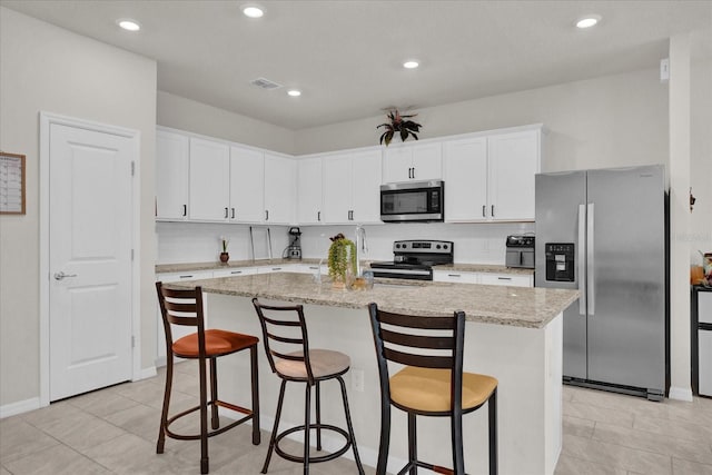 kitchen with a kitchen breakfast bar, an island with sink, stainless steel appliances, light stone countertops, and white cabinets