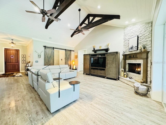 living room with ceiling fan, a barn door, light hardwood / wood-style flooring, ornamental molding, and a fireplace