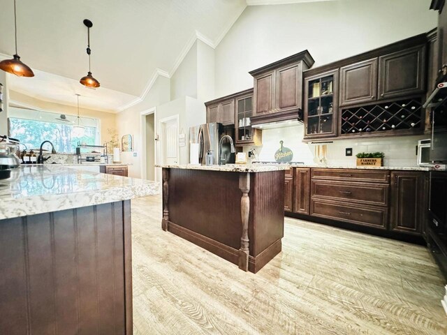 kitchen with light stone countertops, a kitchen island, dark brown cabinetry, vaulted ceiling, and decorative light fixtures