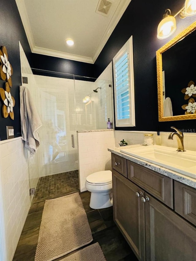 bathroom with tile walls, toilet, a shower with shower door, vanity, and crown molding