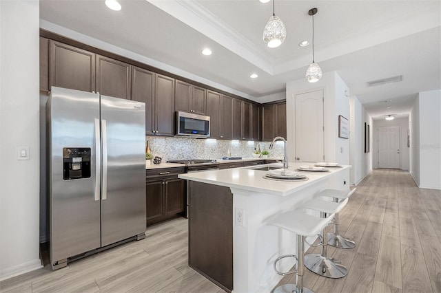 kitchen with a center island with sink, hanging light fixtures, light hardwood / wood-style floors, and stainless steel appliances