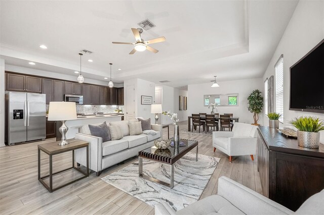 living room with light hardwood / wood-style flooring, a raised ceiling, ceiling fan, and sink