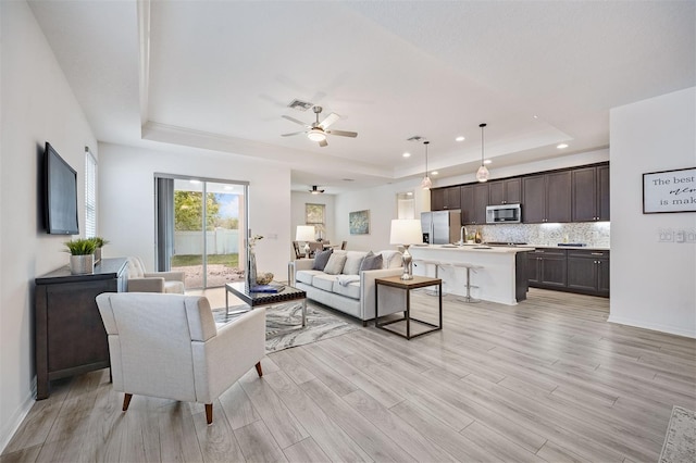 living room with light wood-type flooring, ceiling fan, a raised ceiling, and sink