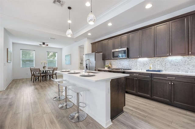 kitchen featuring crown molding, stainless steel appliances, light wood-type flooring, pendant lighting, and a kitchen island with sink