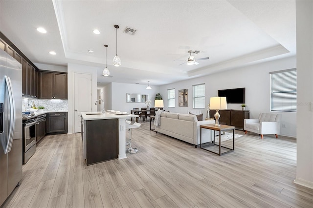 kitchen featuring a center island with sink, light wood-type flooring, appliances with stainless steel finishes, and a tray ceiling