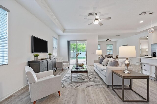 living room featuring ornamental molding, light hardwood / wood-style flooring, ceiling fan, and a tray ceiling