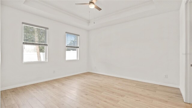 spare room with ornamental molding, light hardwood / wood-style floors, ceiling fan, and a tray ceiling