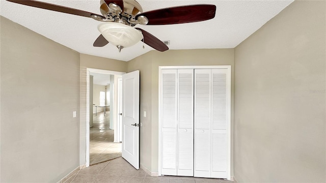 unfurnished bedroom with light tile patterned flooring, a textured ceiling, ceiling fan, and a closet