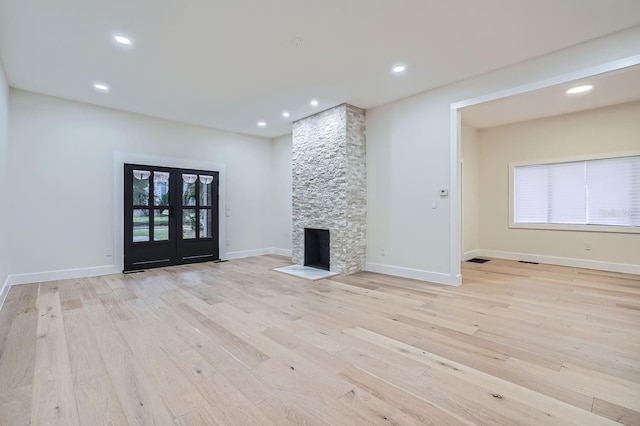 unfurnished living room featuring french doors, a stone fireplace, and light hardwood / wood-style flooring