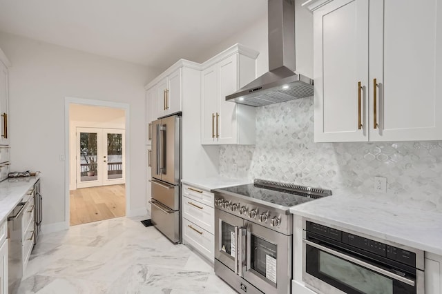 kitchen with wall chimney exhaust hood, backsplash, premium appliances, white cabinetry, and light stone counters