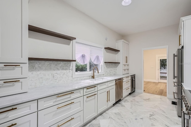 kitchen with tasteful backsplash, appliances with stainless steel finishes, white cabinetry, light stone countertops, and sink