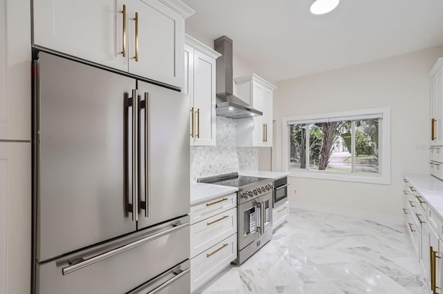 kitchen with wall chimney exhaust hood, white cabinets, tasteful backsplash, and premium appliances