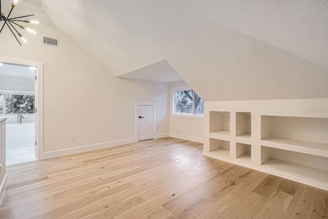 additional living space featuring light wood-type flooring, a textured ceiling, built in features, lofted ceiling, and a notable chandelier