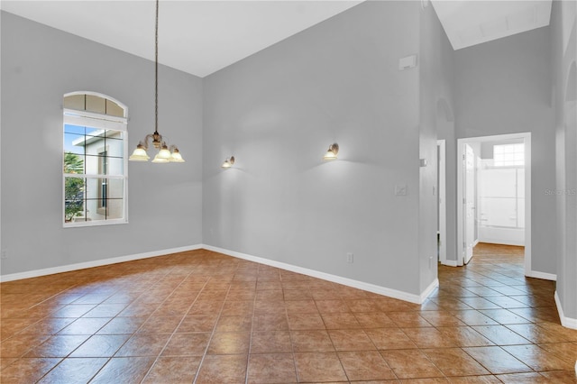 empty room with high vaulted ceiling, tile patterned floors, and a notable chandelier