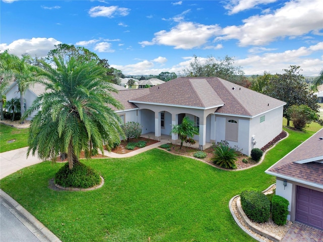 view of front facade with a shingled roof, a front yard, driveway, and stucco siding