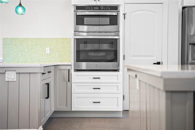 kitchen featuring pendant lighting, decorative backsplash, double oven, and white cabinets