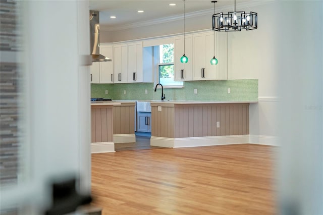 kitchen featuring crown molding, backsplash, white cabinets, wall chimney exhaust hood, and light hardwood / wood-style flooring