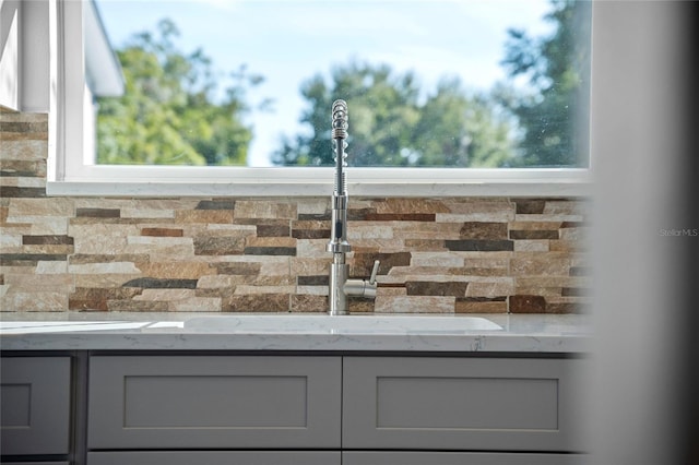 room details with gray cabinetry, tasteful backsplash, and light stone counters