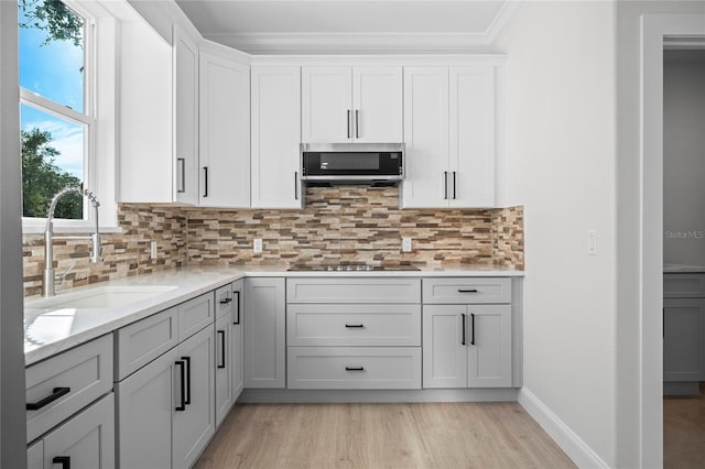 kitchen featuring light hardwood / wood-style floors, black electric stovetop, decorative backsplash, sink, and crown molding